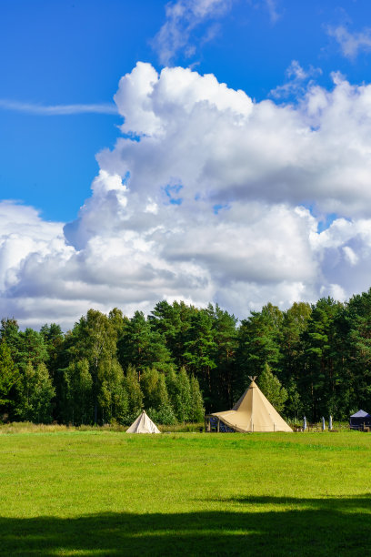 帐篷在森林里，草地上有绿色的草和多云的天空。图片下载