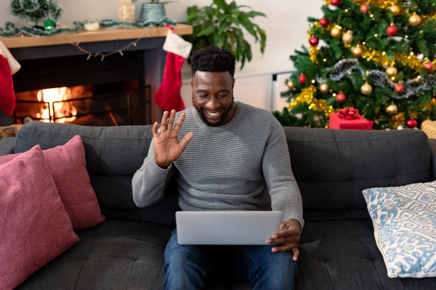 快乐的非裔美国人坐在沙发上，视频通话，圣诞装饰背景图片下载