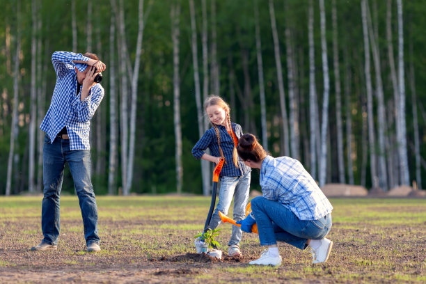这家人正在进行场地美化，在一片小草坪上种植灌木。父亲给他的妻子和女儿拍照。图片下载