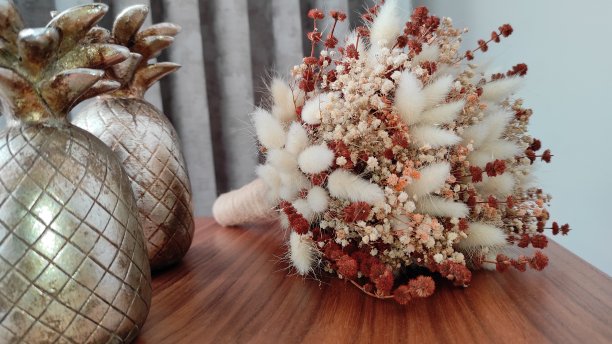 木制茶几上的白色假花、金属菠萝物件和织物窗帘背景图片下载