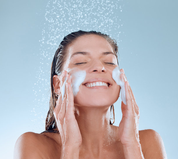 一名年轻女子在淋浴时洗脸，背景为蓝色图片下载