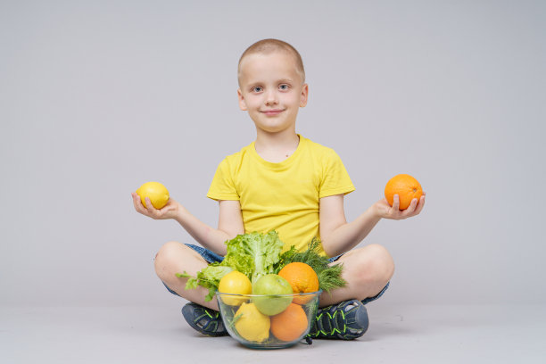 微笑的男孩站在水果和蔬菜的盘子，孤立的灰色图片下载