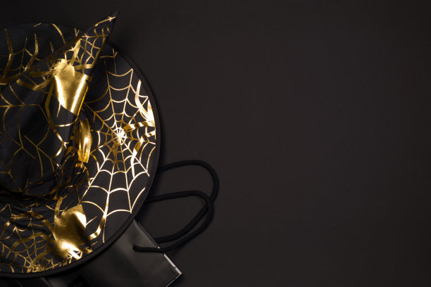 万圣节的节日购物。带蜘蛛网和蜘蛛图案的黑色女巫帽，黑色背景上的购物袋，平放。副本的空间。图片下载