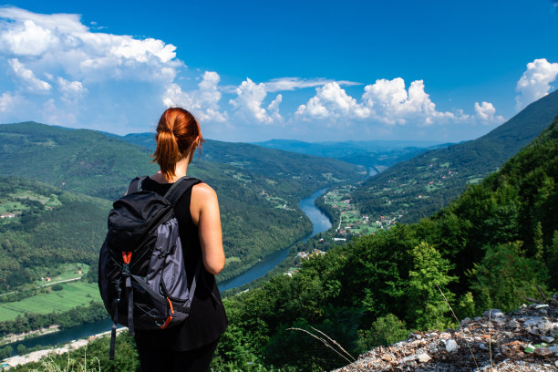 背着背包的女性徒步者站在山顶的后视图。图片下载