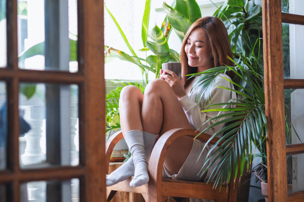 一个年轻的女人喝着热咖啡，在有室内植物花园的阳台上放松图片下载