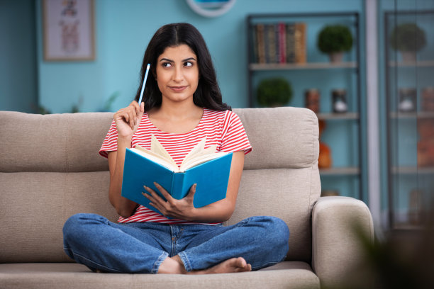 一个女人在家里的沙发上看书。库存图片图片下载