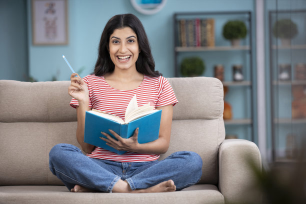 一个女人在家里的沙发上看书。库存图片图片下载