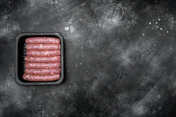 生肉香肠包装盒，在黑色的深色石头桌子背景，顶部视图平铺，与文本复制空间图片下载