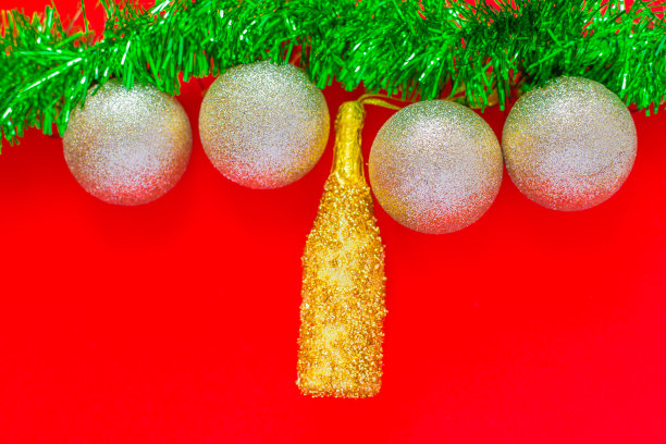 照片的顶部是红色背景，银色的圣诞球和金色的香槟瓶挂在一个绿色的金黄色的毛茸茸的花环上。俯视图，平铺，复制空间，隔离图片下载