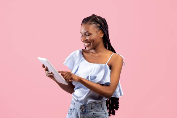 在线生活。漂亮的年轻的非洲女士使用平板电脑远程工作或粉红色工作室背景教育图片下载