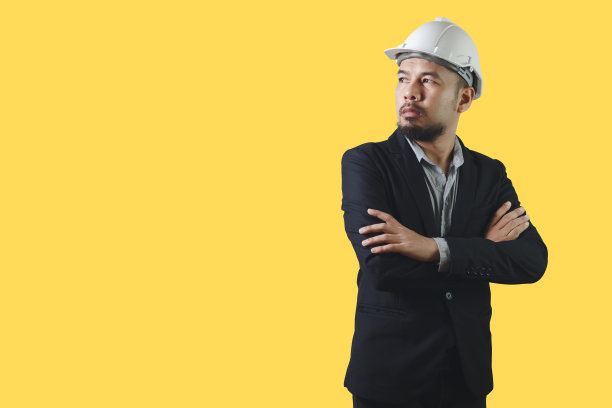 亚洲工程男子穿着黑色西装交叉手臂白色安全帽孤立在黄色背景。工头控制建设。剪切路径。图片下载