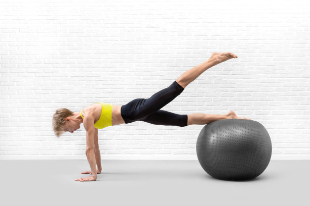 用大的健身球锻炼。苗条的白人女子在室内健身房里用一条腿向上练习平板支撑。图片下载