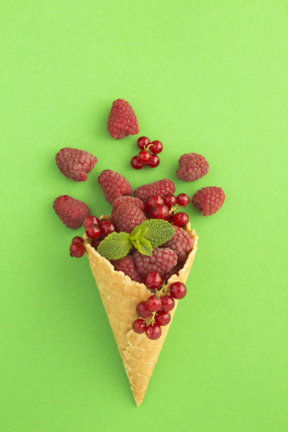 绿色背景中央有覆盆子和红醋栗的冰淇淋蛋筒。前视图。图片下载