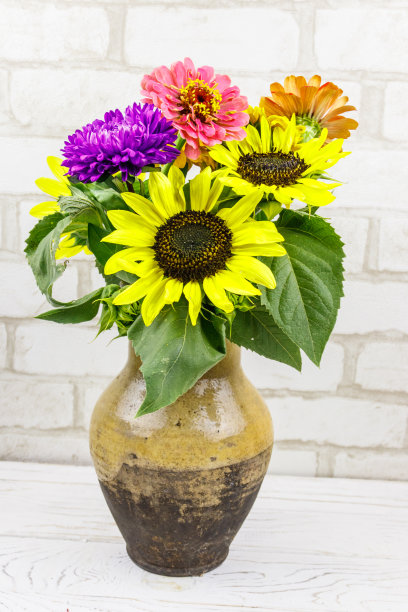 花束放在古色古香的陶罐里，衬着白色砖墙图片下载