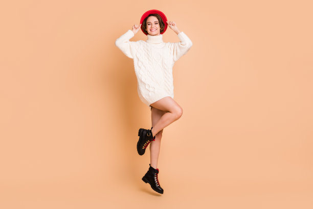 全身照片正面有吸引力的年轻女士跳起来空气穿红色帽子孤立在柔和的米色背景图片下载