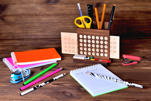 棕色木制背景上有彩色铅笔笔记本、日历和订书机。在记事本上写着“爱”图片下载