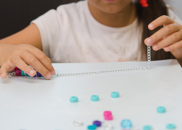 小女孩正从创意包里把蓝色和粉色的珠子串在链子上。精细运动技能，儿童发展。特写镜头。模糊的概念图片下载