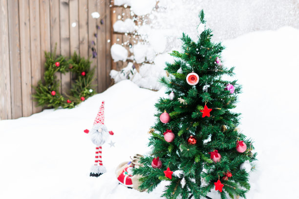 人造冷杉树装饰圣诞节红色玩具在户外院子在雪的背景与装饰的自然冷杉树枝的花环图片下载