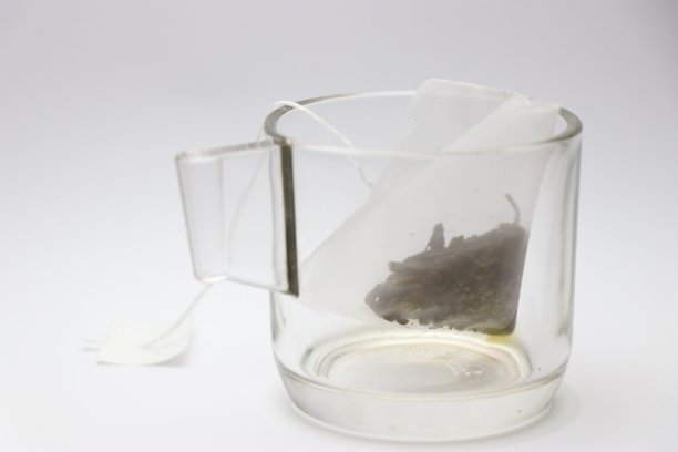 玻璃茶杯与绿茶袋，新鲜草药覆盖非常薄的网袋放置在杯中白色的背景图片下载