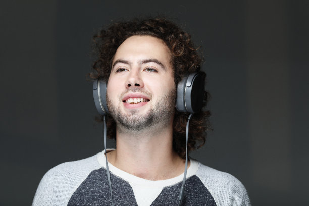 快乐的年轻人微笑着戴着耳机听音乐。在灰色背景图片下载