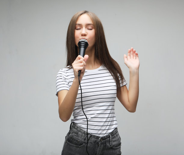 美丽的模特女孩歌手与麦克风在浅灰色的背景图片下载