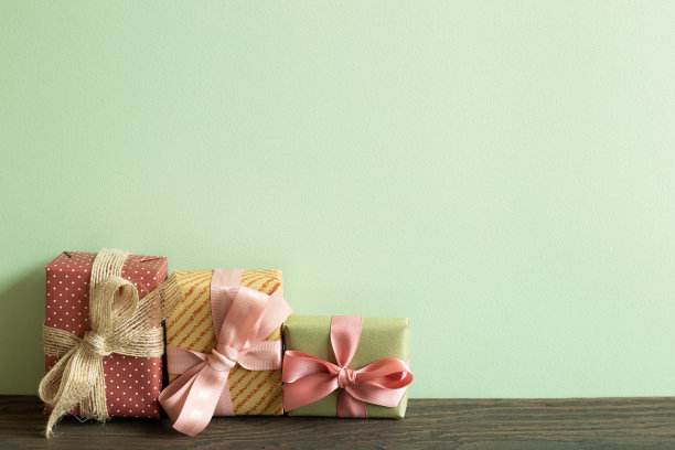 木桌上五颜六色的礼品盒。绿色背景墙图片下载