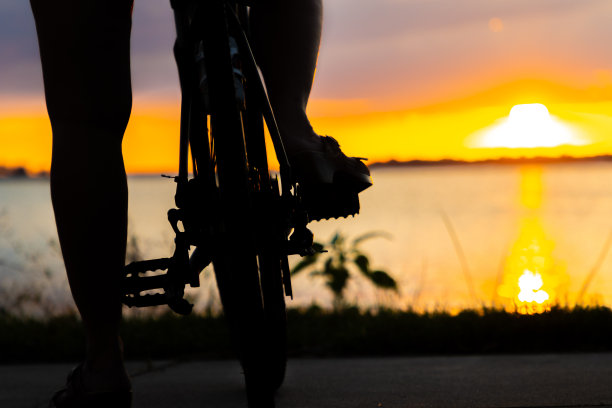 在湖上日落时，双腿和脚踩在自行车踏板和车轮上图片下载