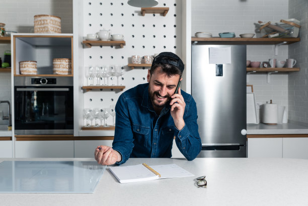 年轻成功的自由职业者，站在现代厨房的家里，用智能手机和快递公司聊天，作为一个满意的顾客，他总是会从他们那里订购图片下载