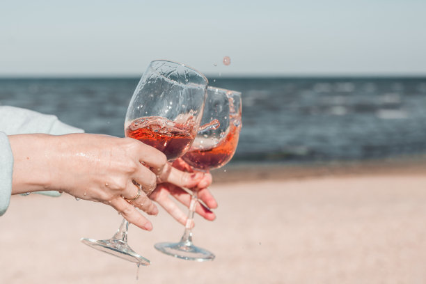 两杯玫瑰酒在女人的手中，在天空和海岸的衬托下。图片下载