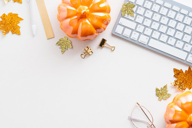 秋天的书桌桌上有键盘、南瓜、白色背景上的眼镜。女性化的工作空间俯视图，舒适的家庭办公桌子。图片下载
