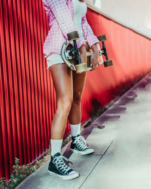 一个溜冰的女孩用她的手握着滑板的裁剪侧视图。那个人已经认不出来了。垂直格式。图片下载