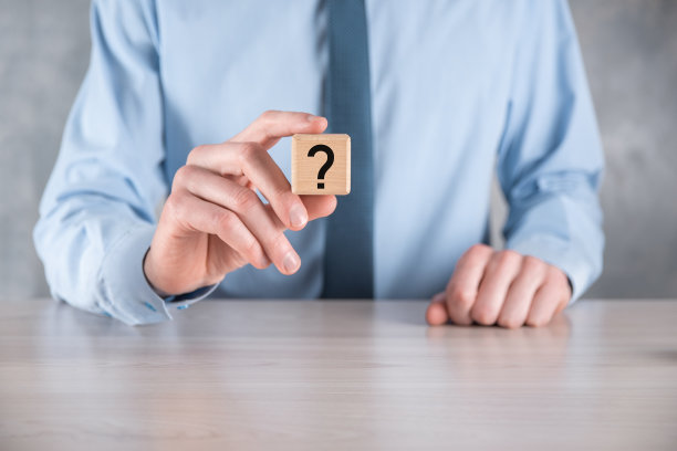 商人手持带有问号的木块放在灰色桌子上。空间的文本。概念的困惑，问题或解决方案图片下载