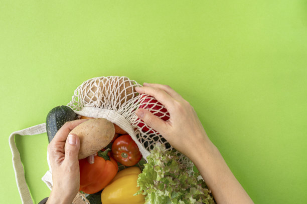 俯视图的女性手伸向有机生态蔬菜从网上购物袋绿色背景。爱护环境，避免塑料概念图片下载