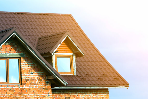 在明亮的蓝天背景下，新砖房顶部有棕色瓦屋顶和塑料阁楼窗户的特写细节。房地产和专业做物业的工作理念。图片下载