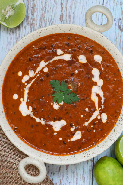 特写图片是kad海风格的碗自制的Dal makhani咖喱食谱，浸泡的黑扁豆，红芸豆与黄油，香草，香料和西红柿泥，淋上奶油，黑纱布，蓝色木纹背景，高架视野图片下载