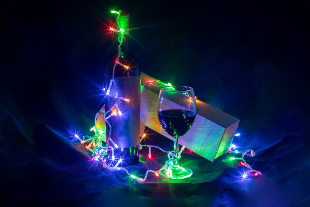 酒杯和酒瓶在闪亮的花环在黑色背景上散景图片下载