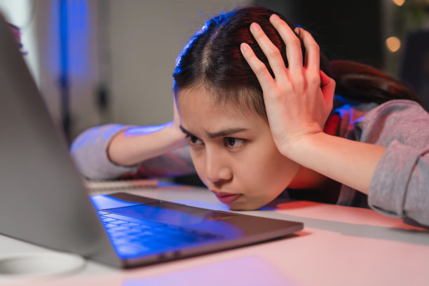 晚上，紧张的亚洲商业女性坐在办公室的椅子上，看着笔记本电脑屏幕。图片下载