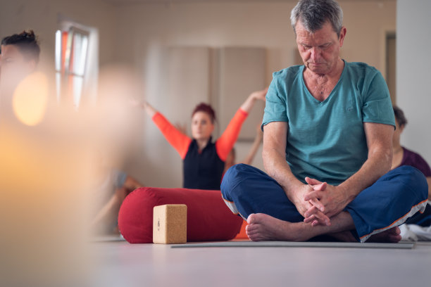 一个成熟的成年男子的全身照片，坐在莲花的位置，冥想，在瑜伽课。图片下载