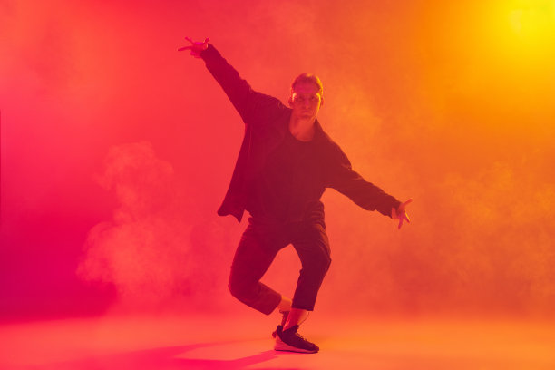 年轻的白人男孩穿着时髦的黑色衣服跳着嘻哈舞，在霓虹灯烟雾中，粉红色的黄色背景下被孤立图片下载
