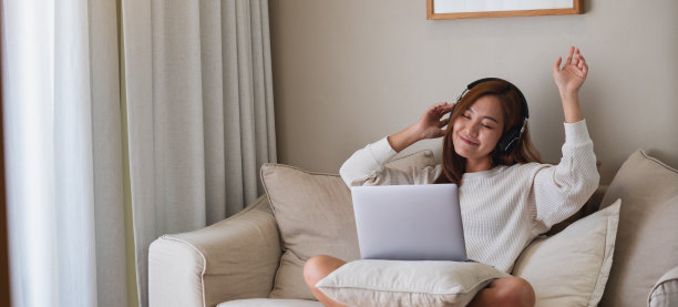 图为，一名年轻女子一边跳舞，一边在家里用耳机和笔记本电脑听音乐图片下载