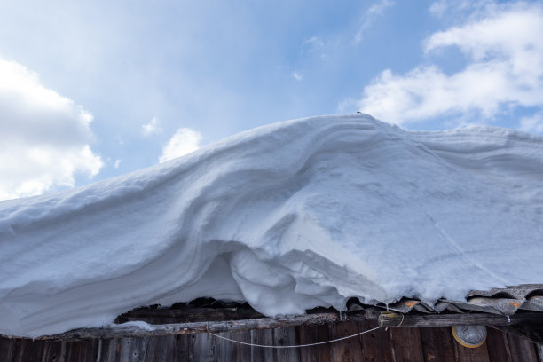 雪堆在屋顶上，映衬着蓝天白云，特写镜头。暴风雪后的雪堆。图片下载