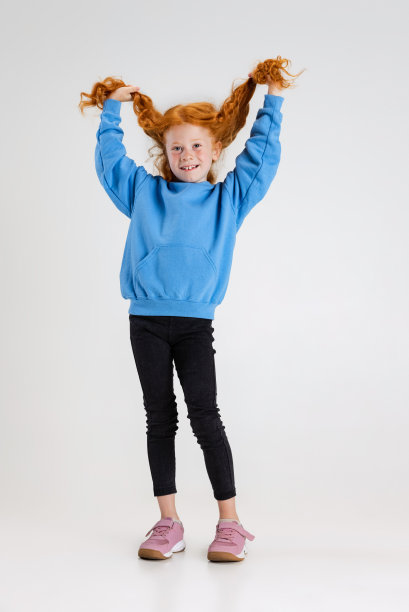 小卷发女孩的全身肖像在蓝色毛衣摆孤立的灰色工作室背景。图片下载