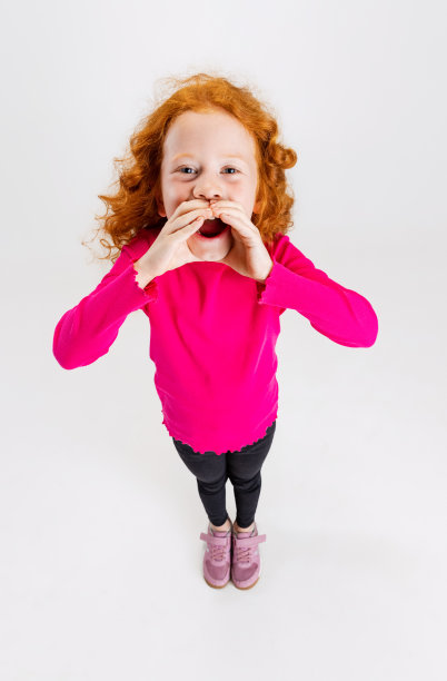 可爱的小红发女孩的肖像在粉红色的天气与手的眼睛孤立在白色的工作室背景。图片下载