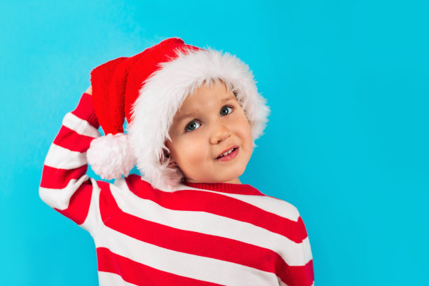 戴着圣诞老人帽子的有趣的孩子，蓝色背景。节日，传统，圣诞节的概念。图片下载