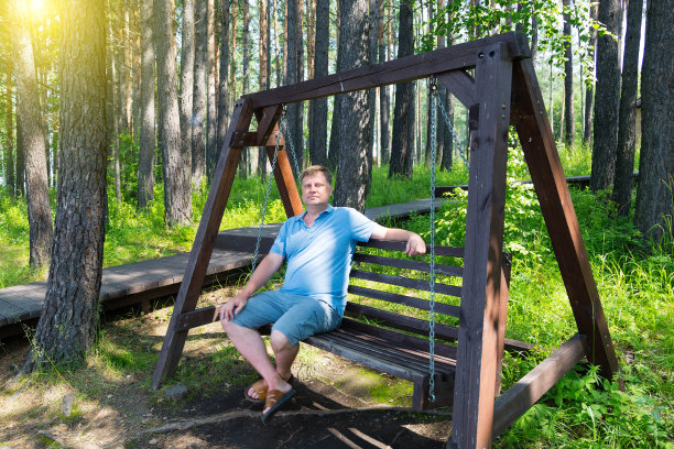 一个成年男子的肖像，在一个夏天的一天，在公园的木秋千上休息图片下载