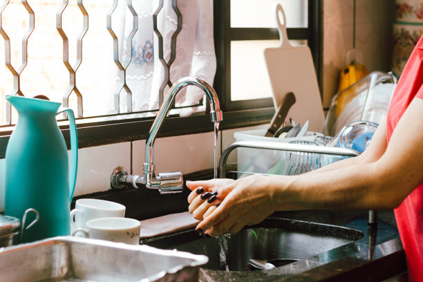 在这张插图照片中，一个女人在满是脏盘子的水槽里洗手图片下载