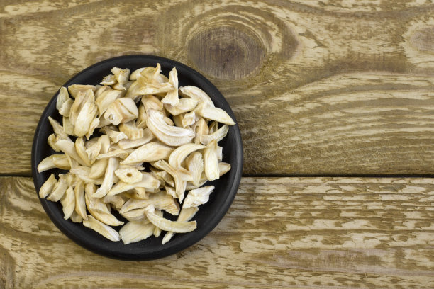 干蒜片在黑色盘子上近距离平铺照片在白色纹理的木制背景图片下载