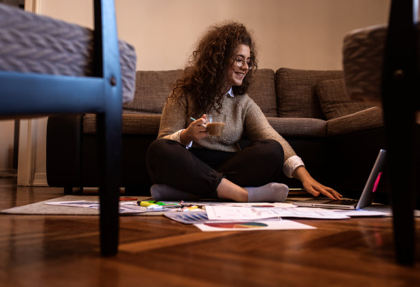 年轻女子坐在地板上在家工作。图片下载