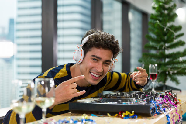 快乐自信的年轻男性DJ戴着耳机，在夜总会的派对上播放混合音乐和在黑胶转盘上旋转。圣诞快乐，节日快乐。庆祝新的一年图片下载