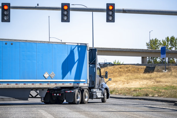 灰色天驾驶室大钻机半挂车与屋顶扰流板运输货物的干货车半挂车在十字路口转弯与交通灯和立交桥道路图片下载